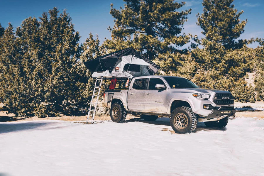Wide-angle view of Body Armor 4x4 Sky Ridge Pike Rooftop Tent set up in snowy forest campsite, rooftop tent for all-season overlanding