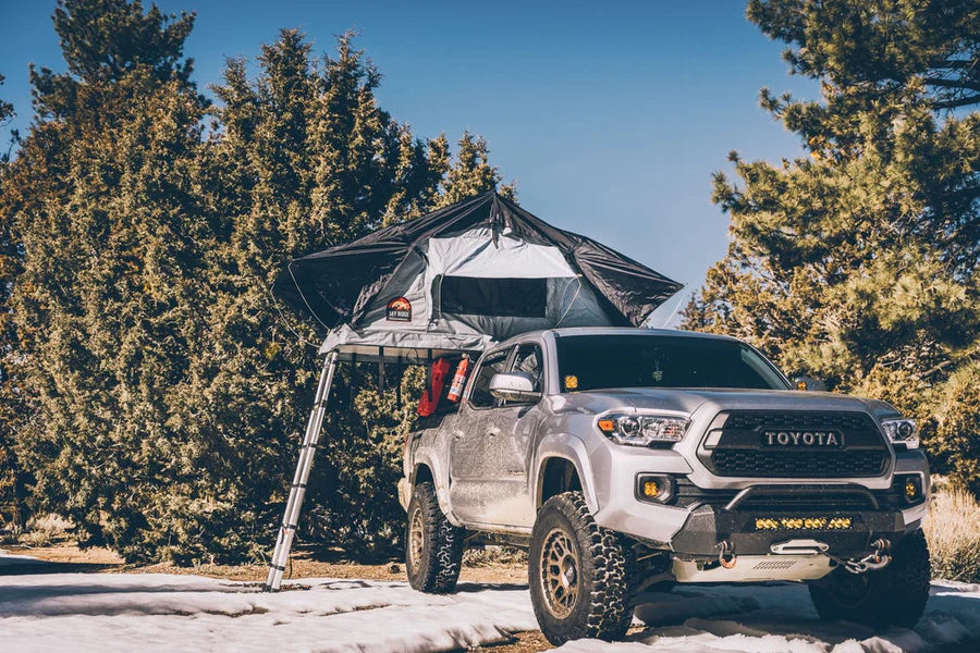 Side view of Body Armor 4x4 Sky Ridge Pike Rooftop Tent mounted on SUV in wooded campsite, showcasing durable rooftop camping solution