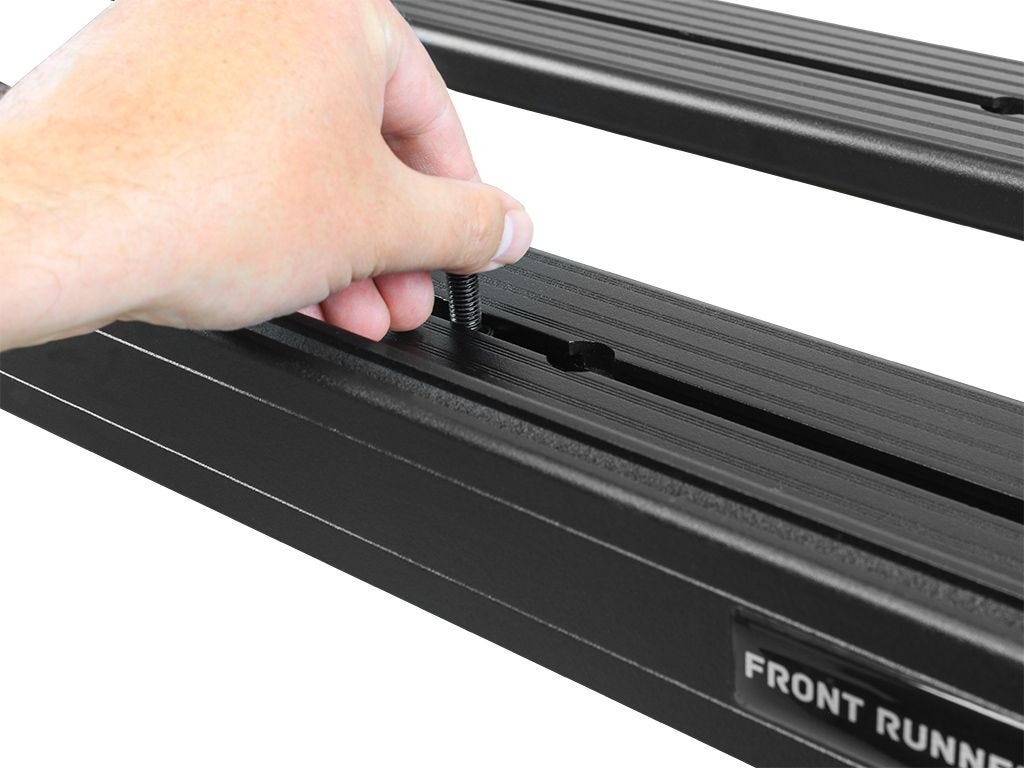 Close-up of hand adjusting FrontRunner Slimline 2 Full Truck Bed Rack Kit rail slot, demonstrating secure mounting system for rooftop tents and accessories