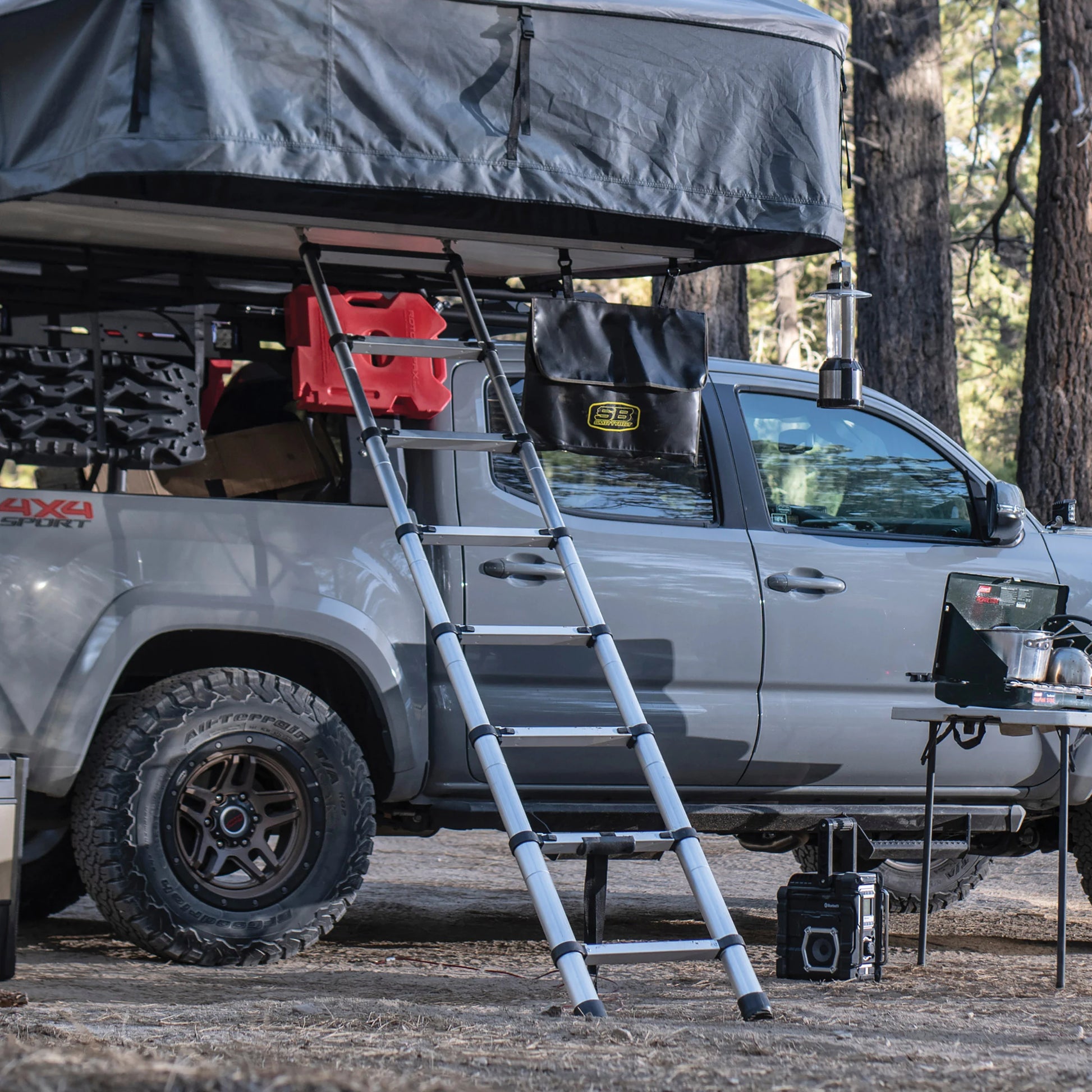 Rear angle of Smittybilt Gen2 Overlander Tent mounted on pickup truck, deployed with ladder extended in forest campsite