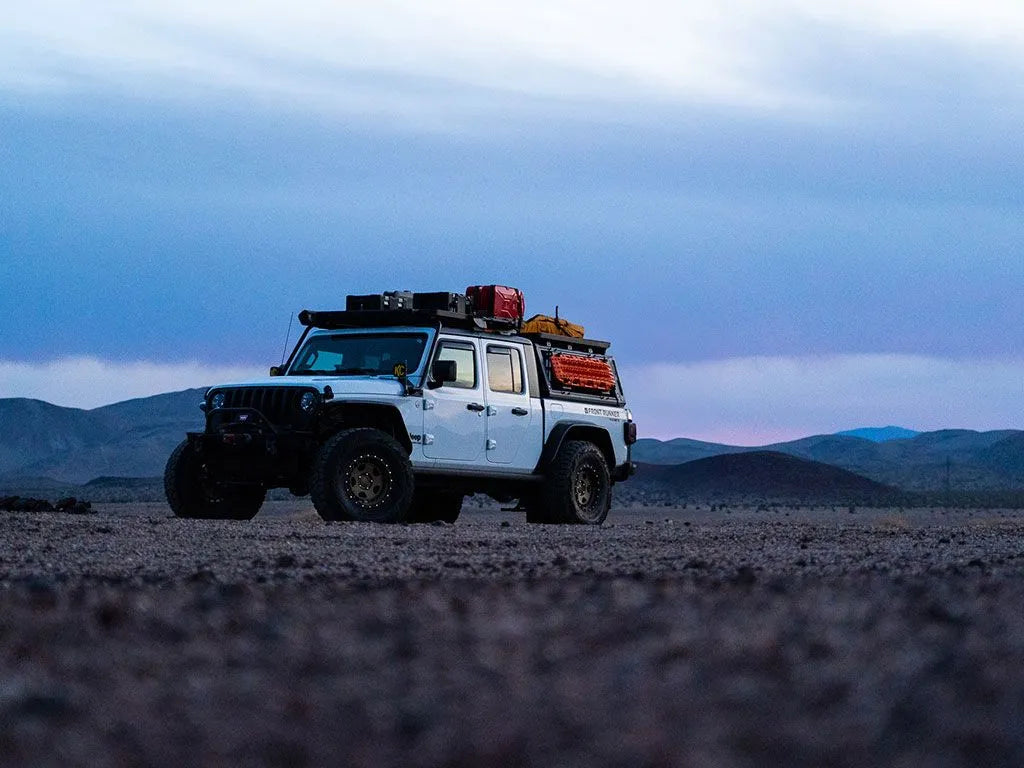 Jeep Gladiator camping at night with FrontRunner Pro Bed Rack Kit and rooftop tent mounted, adventure-ready overlanding setup under starry sky